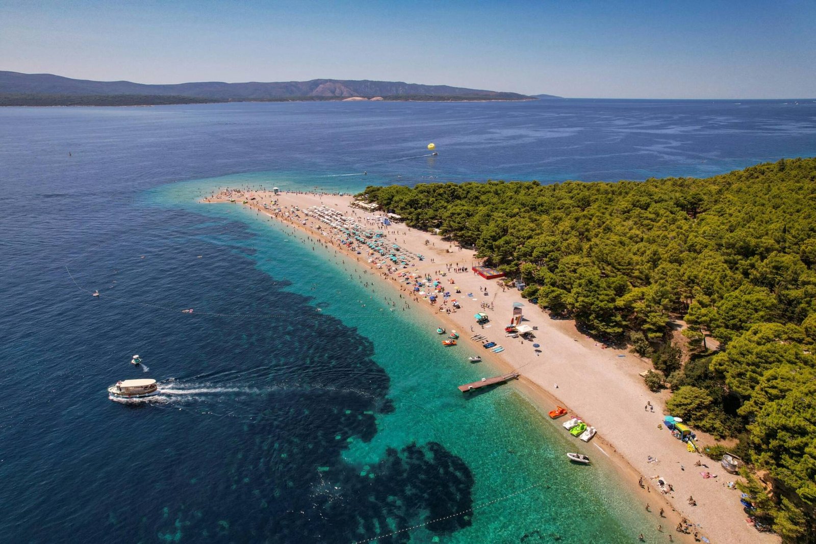 Experience the breathtaking aerial view of Zlatni Rat beach in Bol, Croatia, with clear blue waters and lush green surroundings.