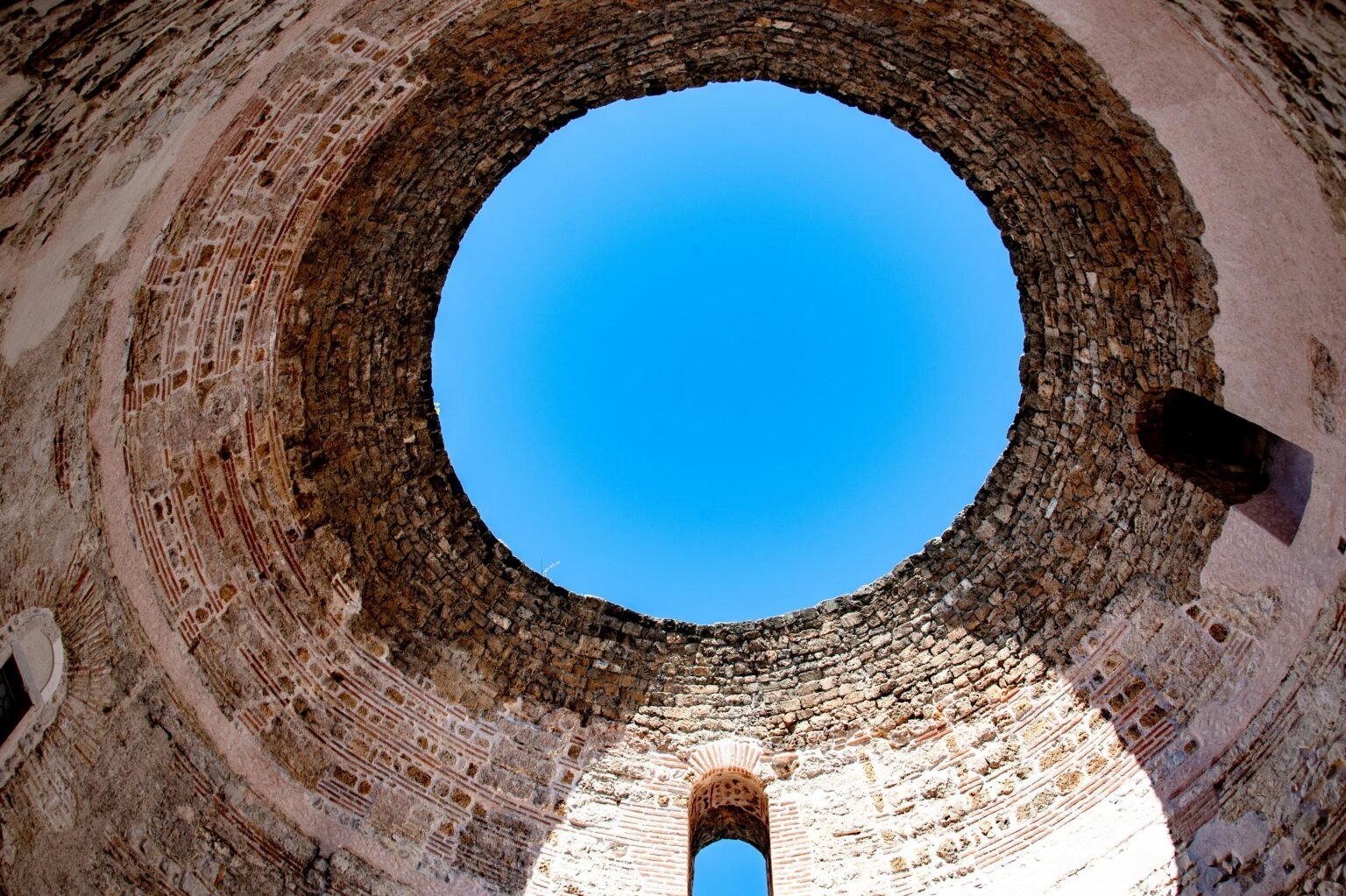 Looking up through the ancient vestibule's circular ceiling in Split, Croatia, under a clear blue sky.